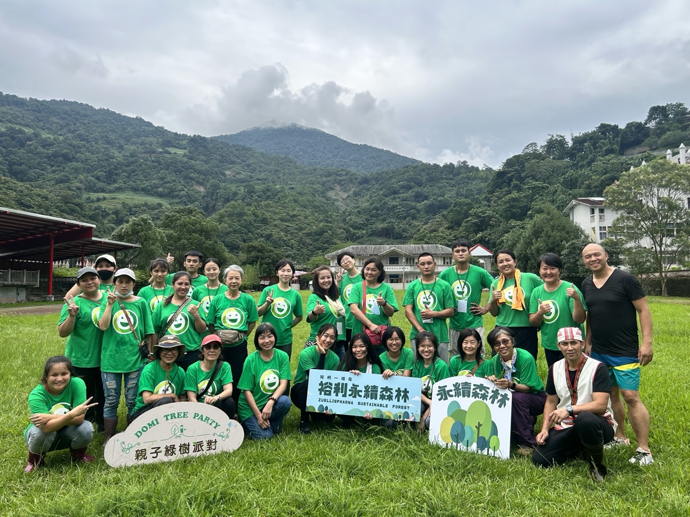 裕利永續森林・親子綠樹派對:員工與家庭穿著 DOMI 綠色 T 恤,在山谷草地上與活動手板合影