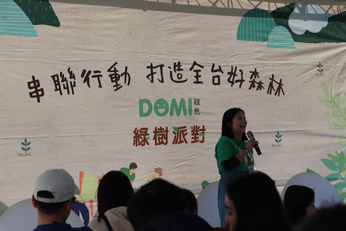 主持人在綠樹派對手繪背板前,為企業參與者開場